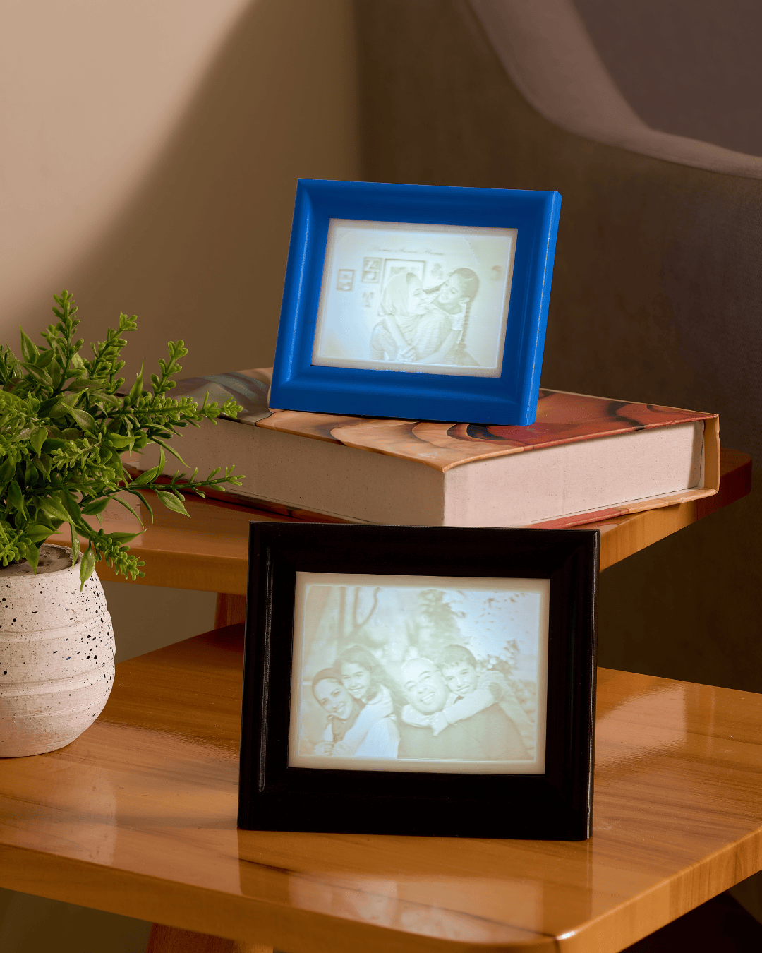 Two digital photo frames, one blue and one black, displaying images on a wooden surface with a plant and book in the background.