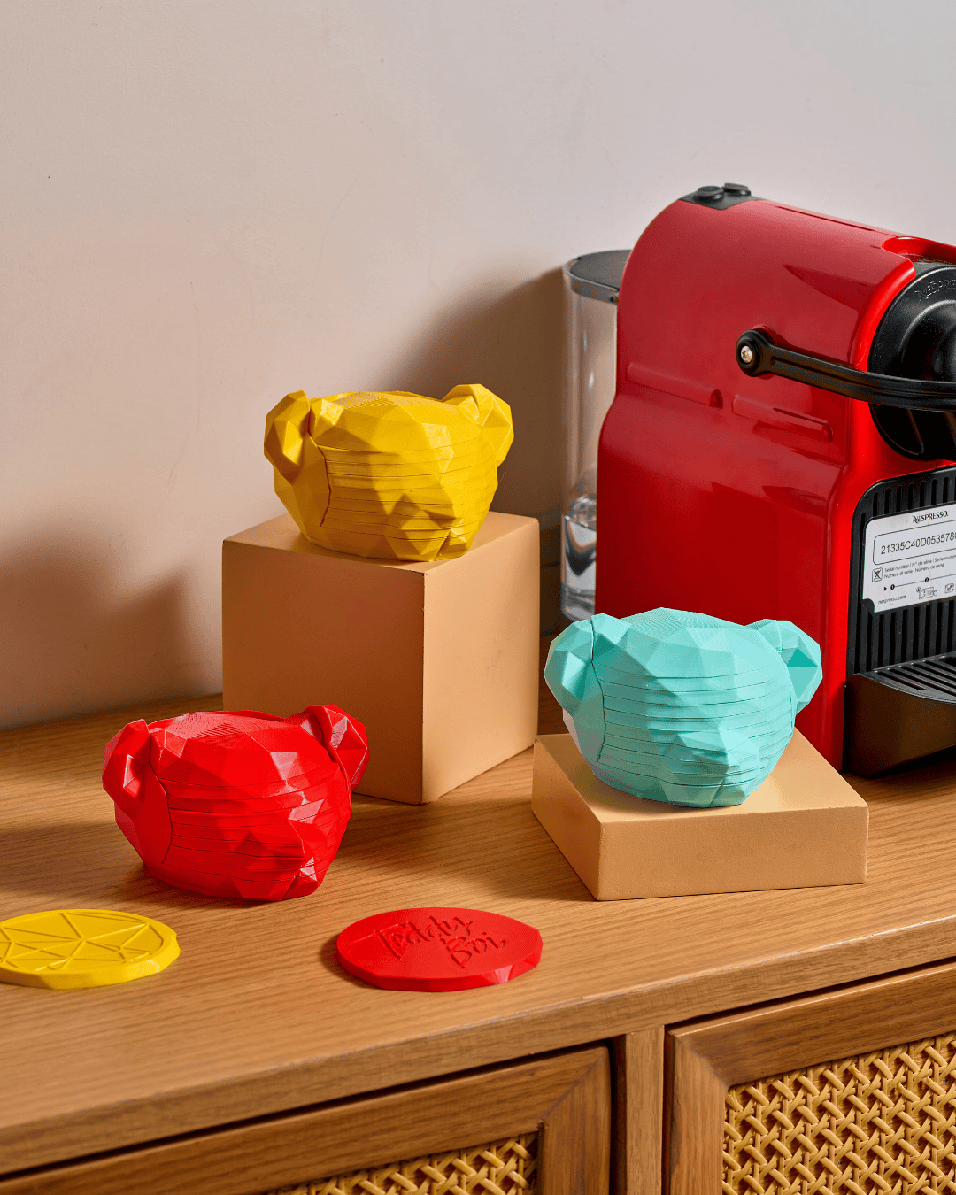 Red espresso machine with colorful 3D-printed bear-shaped items on a wooden surface.